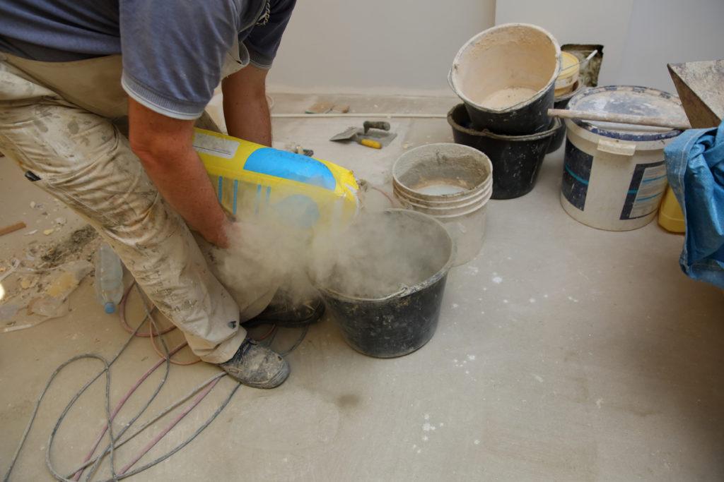 Laborer pouring a bag into a bucket with a plume of dust coming up