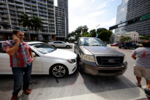 Vehicle collision between a car and truck on Brickell Avenue and 5th Street in Miami. Man on the phone with his personal injury lawyer talking about personal injury protection (PIP).