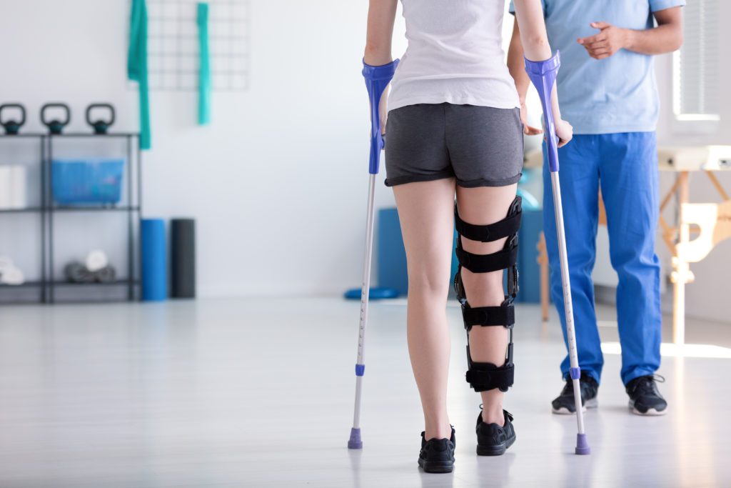 A woman with a leg brace and crutches post-accident bravely works through her therapy exercises.