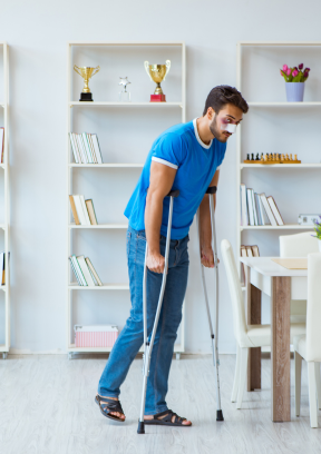 A man, leaning on crutches, carefully navigates with an injured foot.